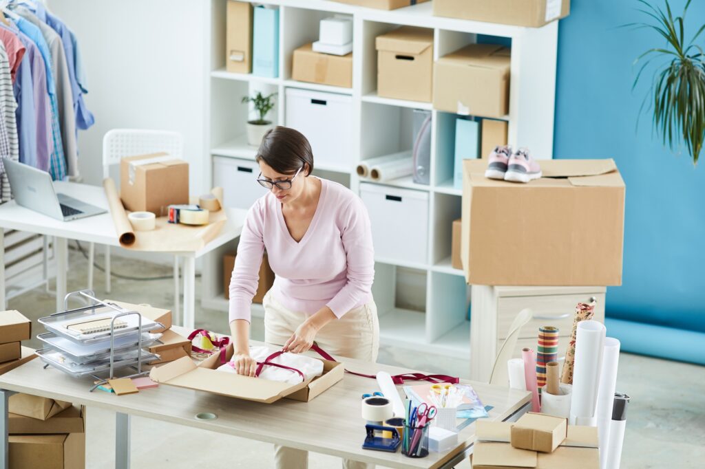Young manager tying silk crimson ribbon around packed online order
