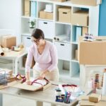 Young manager tying silk crimson ribbon around packed online order